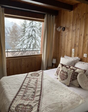 Chambre avec lit brodé et vue sur des sapins enneigés