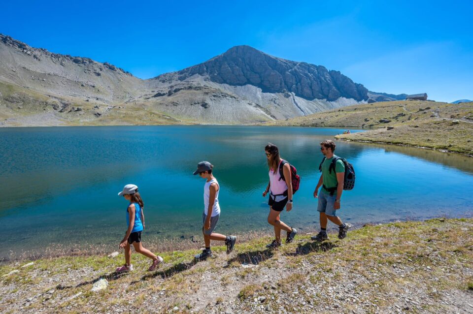 Famille en randonnée au bord d'un lac turquoise du Monde des 6 Lacs à Orcières Merlette